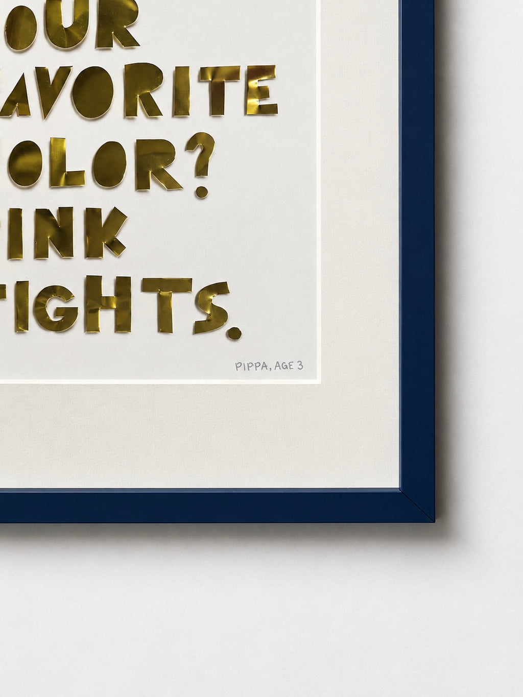 Close-up of a quote piece in a navy frame, gold hand-cut metal letters reading favorite color, pink tights, on white cardstock.