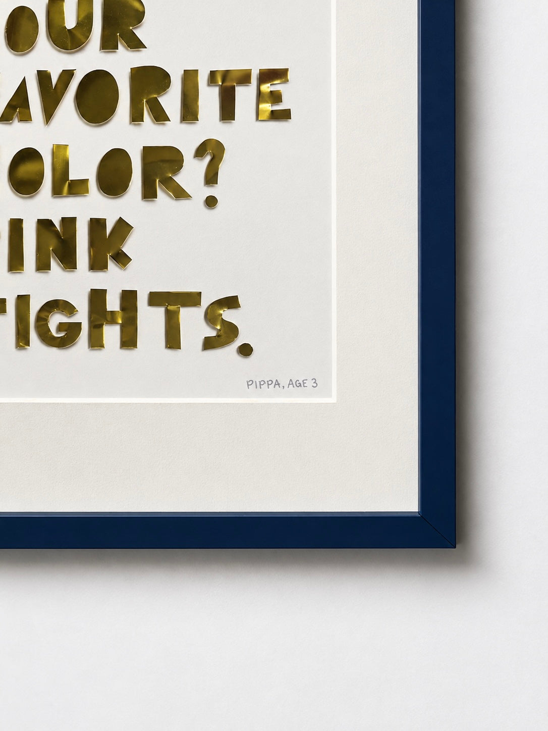 Close-up of a quote piece in a navy frame, gold hand-cut metal letters reading favorite color, pink tights, on white cardstock.