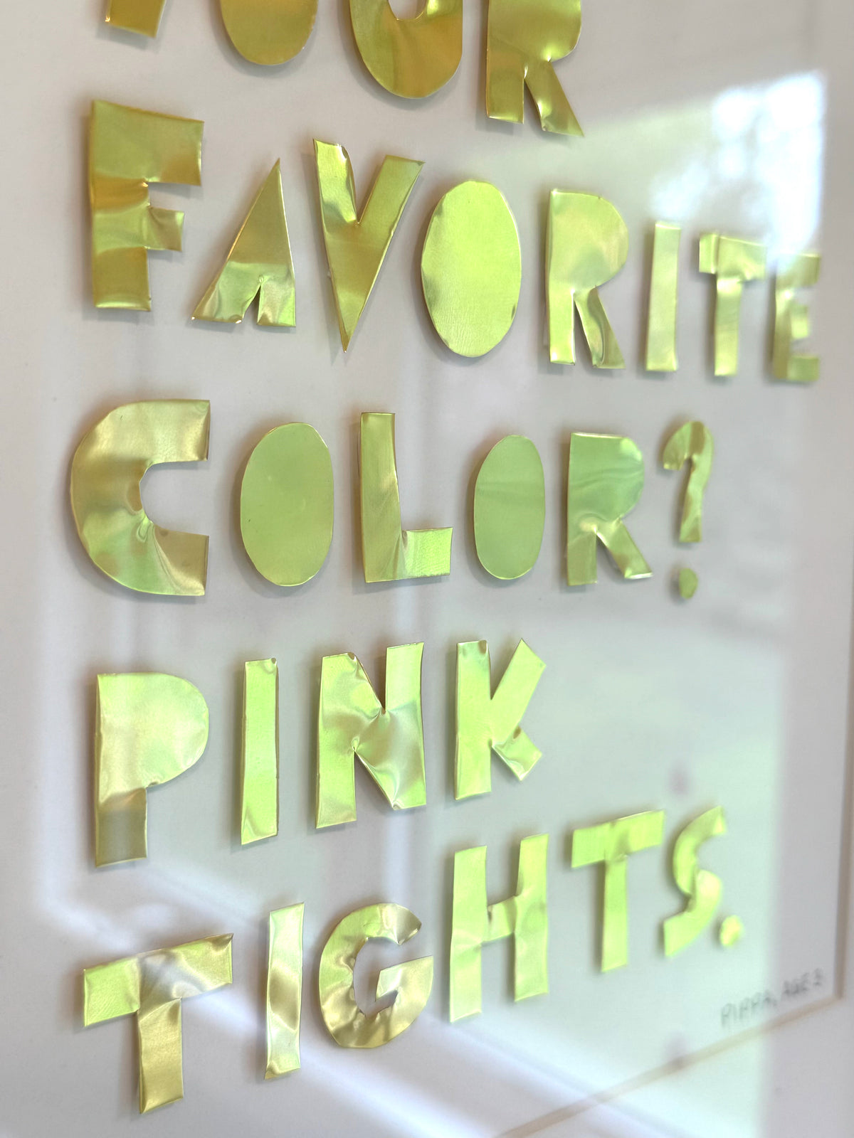 Close-up of gold hand-cut metal letters spelling your favorite color, pink tights, catching the light on a quote piece.