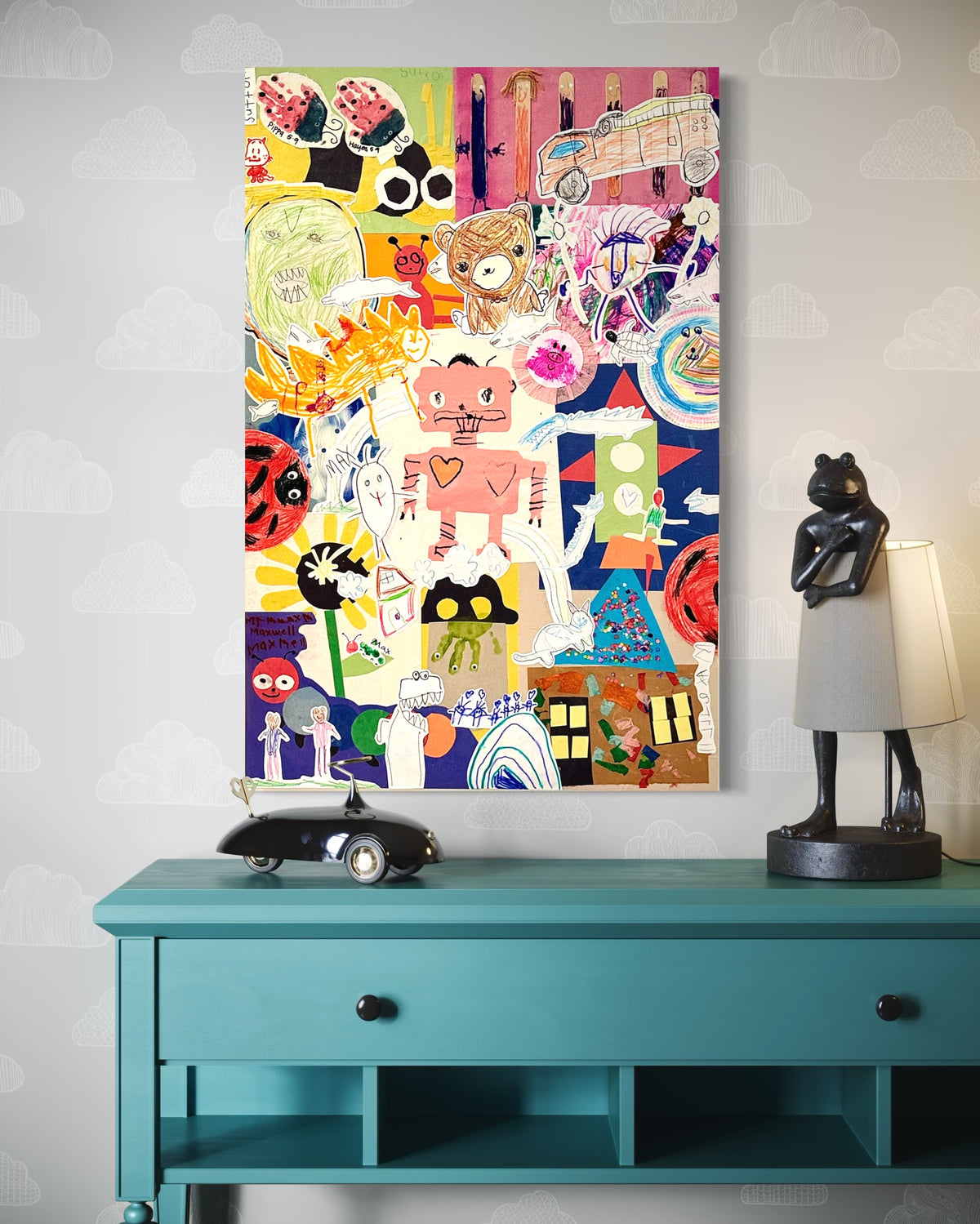 Large custom Pippy + Funk collage hung above a teal console — a child's drawings of a robot, teddy bear, sun, ladybug, and watermelon composed onto cradled basswood, styled with a frog lamp and toy car in a kid's room.