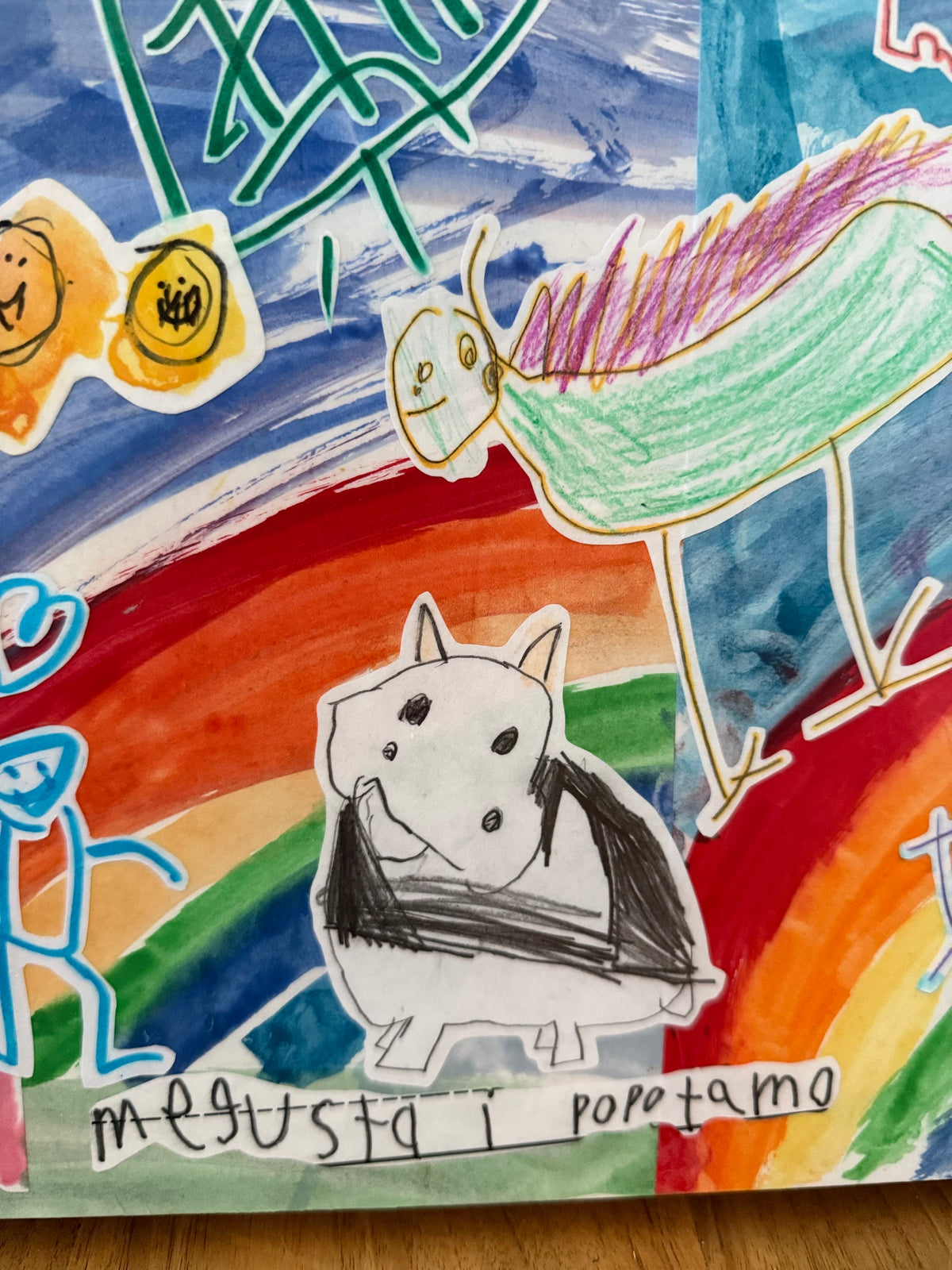 Close-up of a custom collage: a kid's black-and-white animal drawing over a bright rainbow, with their handwriting along the bottom.
