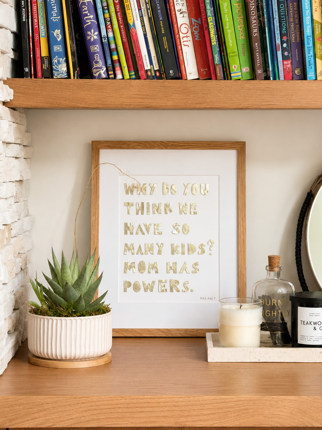 Quote piece styled on a wood shelf beside a plant and books